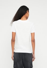 Λευκό βαμβακερό t-shirt με κοντά μανίκια, στρογγυλή λαιμόκοψη και ίσια τελείωμα. Διαθέτει διακριτική ετικέτα της μάρκας στο πλάι. Απλό σχέδιο.