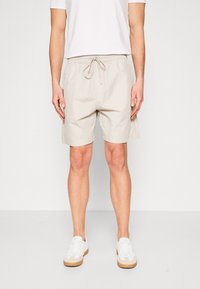 Lichtbeige shorts met trekkoord in de taille, met een eenvoudig ontwerp en een gladde textuur. Gecombineerd met witte sneakers en een eenvoudige witte t-shirt.