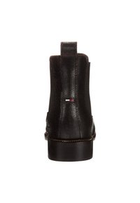 Bota de tobillo de piel negra con tirador, tacón bajo y pequeño logotipo rectangular en rojo, blanco y azul en la parte trasera.