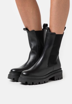 Black leather ankle boots with elastic side panels, rounded toe, and thick lug sole for traction. Features pull tabs for easy wear.