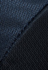 Strukturierte Stoffe in Blau- und Schwarztönen, die ein geometrisches Muster mit einer glatten Oberfläche und einem kontrastierenden dunkleren Bereich aufweisen.