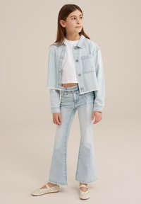 Light blue cropped denim jacket with button closure and one pocket, paired with light blue flared jeans. Features a white short-sleeve top.