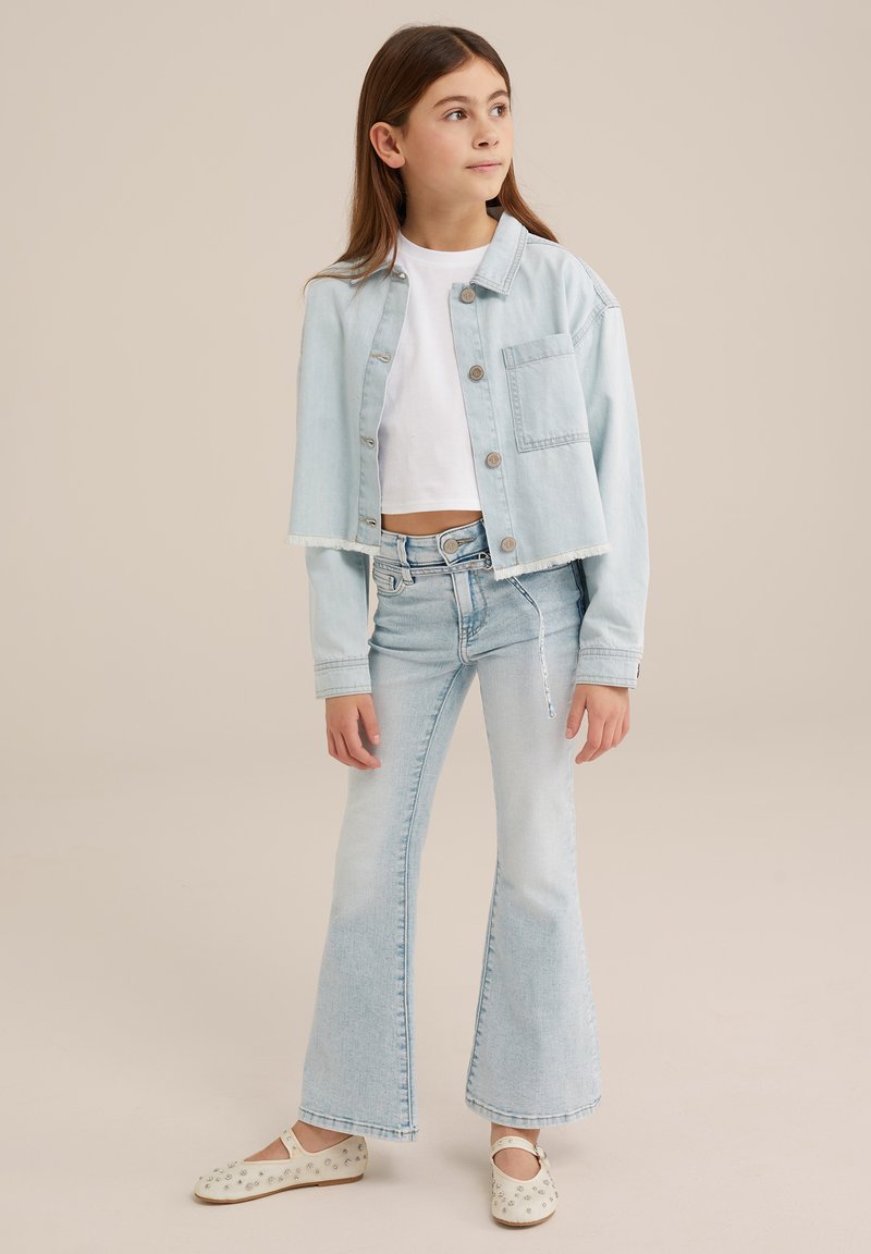 Light blue cropped denim jacket with button closure and one pocket, paired with light blue flared jeans. Features a white short-sleeve top.