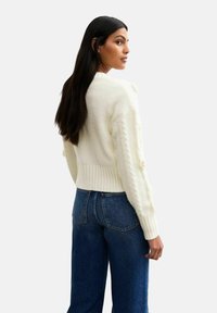 Maglione bianco lavorato a maglia con orlo a coste, dettagli a trecce sulle maniche e vestibilità rilassata, abbinato a jeans blu a vita alta.