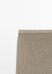 Tissu tricoté beige plié au bord supérieur sur fond blanc, montrant des points fins, uniformes et une texture.