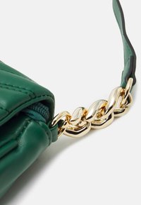 Zielona skórzana torba o pikowanym wzorze, z złotym metalowym uchwytem łańcuchowym i czarnym akcentem na pasku.