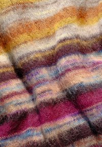 Primo piano di un tessuto morbido e vellutato con strisce orizzontali nei toni del giallo, arancione, viola, rosa, blu e beige, che mostra la texture e le pieghe.