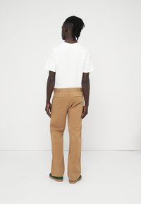 Καφέ παντελόνι με ίσια γραμμή, κατασκευασμένο από βαμβακερό ύφασμα· συνδυασμένο με απλό λευκό μπλουζάκι, από πίσω.