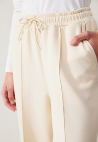 Beige joggers med ett elastiskt midjeband och dragsko, med sidofickor och en slät, mjuk textur.
