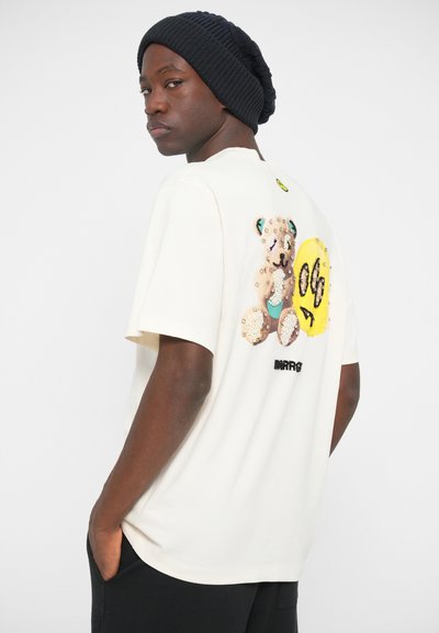 Cream short-sleeve t-shirt featuring a bear and smiley face graphic on the back, embellished with sequins and a round neck design.