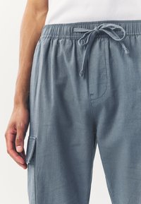 Light blue cargo pants with an elastic waistband and drawstring, featuring a side pocket and a smooth, textured fabric.