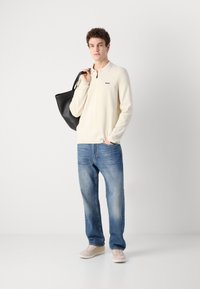 Cream long-sleeve polo with a zip collar and a 'BOSS' logo, paired with loose blue denim jeans and light beige sneakers, carrying a black tote bag.