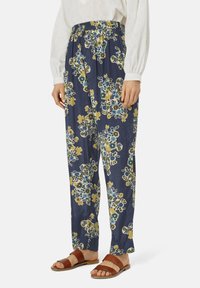 Pantaloni stampati floreali in navy con motivi gialli e blu; vita elastica; tessuto leggero; vestibilità ampia; abbinati a sandali marroni.