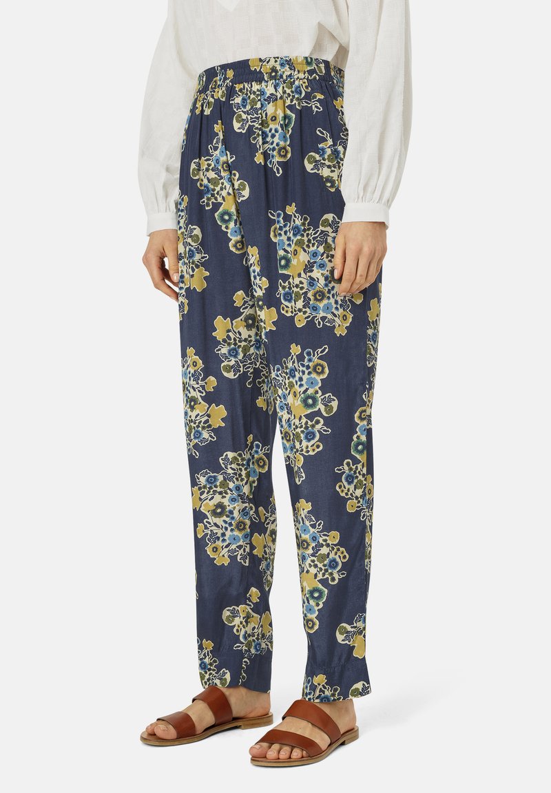 Pantaloni stampati floreali in navy con motivi gialli e blu; vita elastica; tessuto leggero; vestibilità ampia; abbinati a sandali marroni.