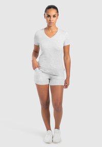 T-shirt grigio con scollo a V e maniche corte abbinato a pantaloni Corti grigi dello stesso colore. Il tessuto sembra morbido, con una texture liscia. Scarpe da ginnastica bianche.