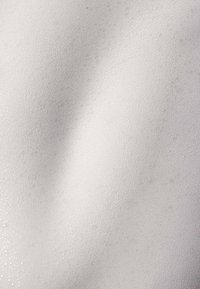 White foam material with a smooth texture, featuring small, uniform bubbles and a subtle sheen across a gently undulating surface.