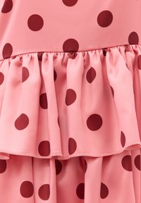 Tissu rose avec des pois rouge foncé, présentant un détail de volant froncé et un design superposé.