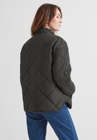Quilted black jacket with a stand collar and diamond pattern, paired with blue jeans. Smooth texture, loose fit, and no visible hardware.