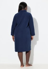 Tmavě modrý fleecový župan s dlouhými rukávy, klopovým límcem a délkou sahající ke kolenům. Hladká textura a jednoduchý střih.