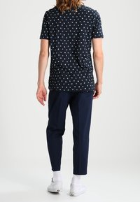 Camisa de manga corta en color navy con un patrón circular repetido en azul claro, combinada con pantalones ajustados de color azul oscuro. Presenta un ajuste relajado y una tela suave.