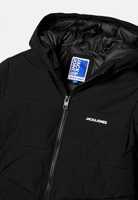 Melna jaka ar kapuci, pūkaina tekstūra, rāvējslēdzēja aizdare un balts uzraksts uz krūškurvja. Iekšpusē ir gluda, spīdīga oderējuma.