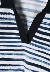 Haut rayé avec un motif bleu marine, blanc et bleu clair, doté d'un col en V et d'un tissu texturé. Des rayures verticales et horizontales sont présentes.