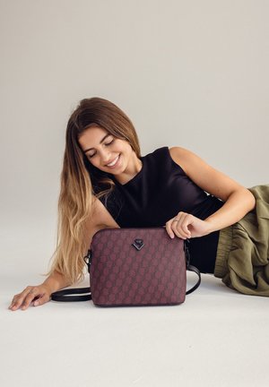 Burgunderfarbige Umhängetasche mit Lederfinish, ausgestattet mit einem Logoakzent und verstellbarem Gurt. Glatte Textur und rechteckige Form.