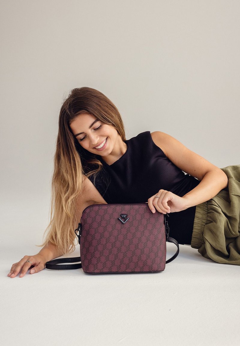 Burgunderfarbige Umhängetasche mit Lederfinish, ausgestattet mit einem Logoakzent und verstellbarem Gurt. Glatte Textur und rechteckige Form.