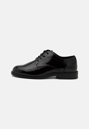 Chaussures habillées en cuir verni noir avec un bout arrondi, un laçage et une surface lisse. Elles ont un petit talon en caoutchouc noir et des détails cousus.