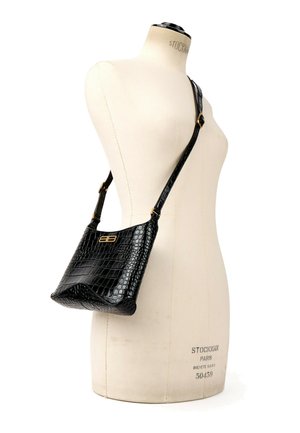 Sort crossbody taske i krokodilleskind med guld dobbel-B-logo på justerbar rem, vist på mannequin torso.