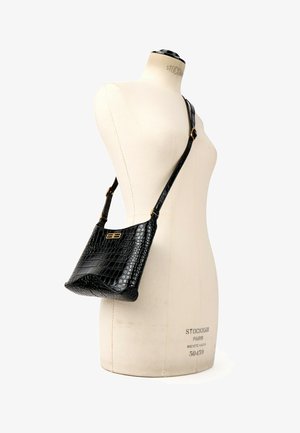 Sac bandoulière en cuir noir à texture crocodile avec logo double-B doré sur une sangle réglable, exposé sur un buste de mannequin.