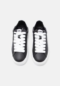 Ténis de couro preto com atacadores brancos, biqueira arredondada, laterais texturizadas e solas de borracha brancas. Etiqueta com logótipo na língua. Design plano e casual.