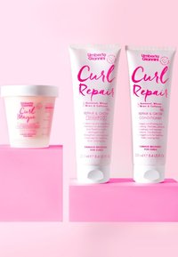 Drie haarverzorgingsproducten met lichtroze verpakkingen: een ronde pot met het label "Curl Magic" en twee tubes met de labels "Curl Repair" shampoo en conditioner.