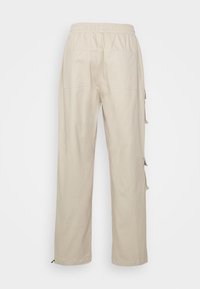 Pantalon beige à taille élastique avec jambes droites, deux poches arrière et détails de lanières latérales visibles sur la jambe droite.