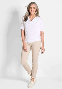 Witte top met korte mouwen en gedrapeerde halslijn, gecombineerd met beige slim fit broek en witte sneakers. Glad materiaal; losse pasvorm.