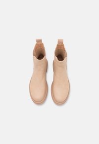 Botines beige de cuero suave con punteras redondeadas, paneles laterales elásticos y tableros de agarre para facilitar su colocación. Suelas de goma planas.