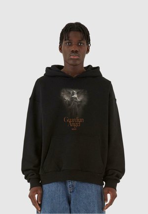 Sort hættebluse med et grafisk motiv af en skytsengel og orange tekst. Har en stor frontlomme og løs pasform. Blød stofstruktur.