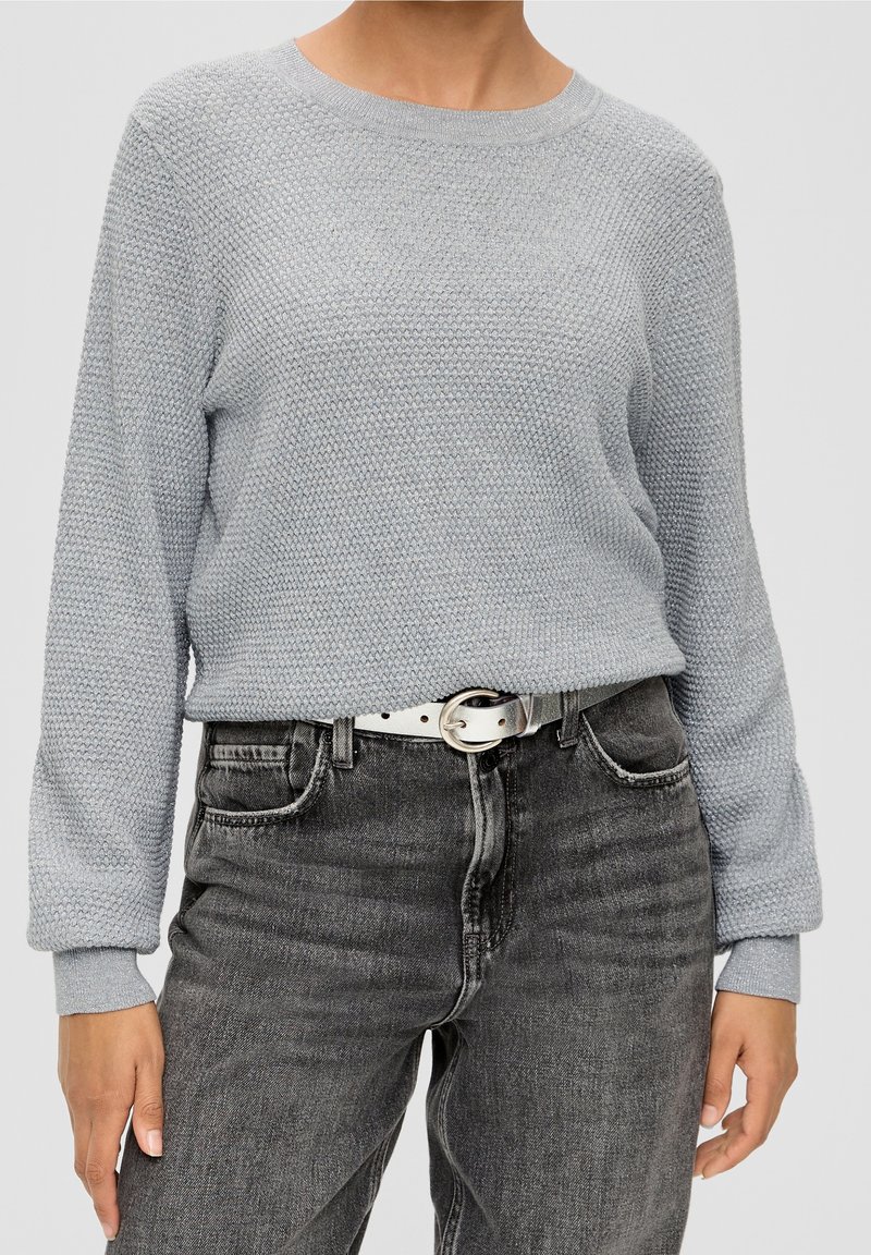Personne portant un pull gris clair texturé rentré dans un jean noir délavé taille haute avec une ceinture en cuir blanc.