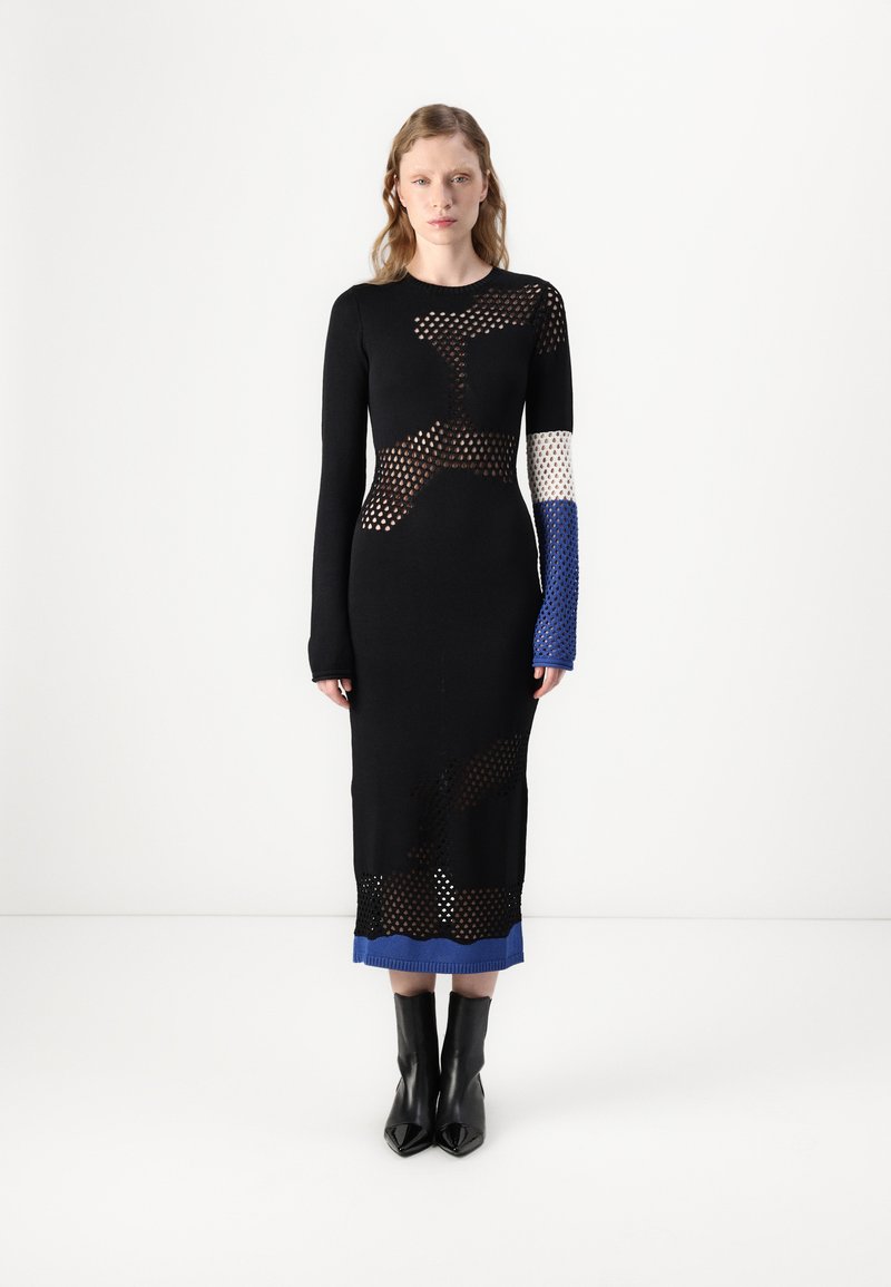 Svart stickad klänning med nätmönster, långa ärmar och blå detaljer vid ärmsluten och fållen. Har en figurnära silhuett med utskärningar.