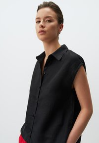 Camicia nera in lino con colletto, maniche corte e chiusura con bottoni, caratterizzata da una vestibilità ampia e una texture morbida.