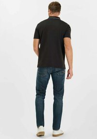 Zwart poloshirt met witte kraagaccenten, gecombineerd met blauwe jeans. Slanke pasvorm, korte mouwen en een soepele stof. Casual schoeisel.