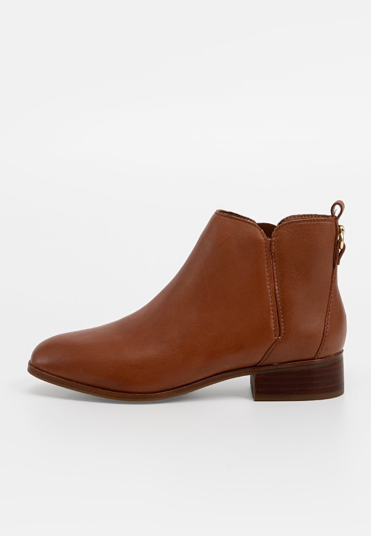 Bottine en cuir marron avec un bout arrondi, une fermeture éclair sur le côté et un petit talon empilé. Texture lisse avec des détails minimes.