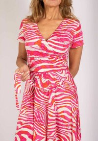 Różowo-biała sukienka w paski zebry z krótkimi rękawami, głębokim dekoltem w serek i paskiem do związania. Gładki materiał, zwiewny krój, intensywne kolory.