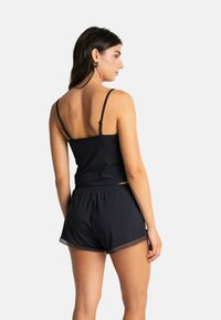 Camisole en coton noir avec des bretelles réglables, associée à un short noir assorti avec une finition en dentelle à l'ourlet. Texture lisse, coupe décontractée.