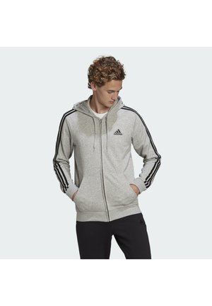 Felpa zip grigia chiara con cappuccio, strisce laterali nere e logo Adidas sul petto. Realizzata in un materiale morbido e testurizzato.