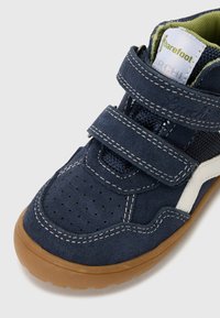 Children's navy suede shoe with white accents, textured mesh panels, two adjustable Velcro straps, perforated toe, and a brown rubber sole.