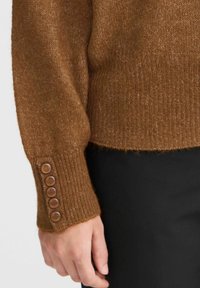Pull en maille marron à texture côtelée et manches évasées, avec cinq boutons beiges sur le poignet et un design court.