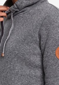 Felpa grigia con tasca a marsupio, cappuccio con cordino e una patch in pelle sulla manica. Texture morbida con vestibilità rilassata.