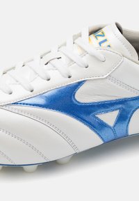 Scarpa da calcio sintetica bianca con dettagli azzurri lucidi, superficie in pelle texturizzata e lacci bianchi con linguetta grigia chiara.