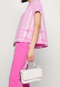 Blusa corta de manga corta color rosa brillante con patrones geométricos, combinada con pantalones rosas. Bolso blanco con un asa de cadena. Textura suave y corte relajado.